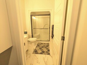 Et aflangt badeværelse med toilet, bruseområde og et mønstret gulv.
