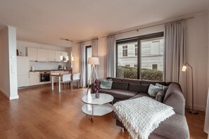 A modern living room with a sofa, coffee table, and lamp. There is a kitchen area with cabinets and a dining table. - Villa Friede-Marie, App. Hannah - with terrace and Baltic Sea view (Sassnitz auf Rügen)