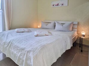 A neatly made bed with a white quilt and floral pillows, a bedside table with a lamp, and a painting on the wall. - Ferienhaus Zum Kreideblick, FeWo Muschel - Holiday home Zum Kreideblick, (Sassnitz auf Rügen)