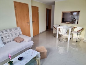 A living room with a sofa, a table with chairs, a kitchen area with utensils, and a door. - Ferienhaus Zum Kreideblick, FeWo Muschel - Holiday home Zum Kreideblick, (Sassnitz auf Rügen)