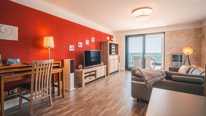 A modern living room with a TV, wooden furniture, and a balcony with a view. - Villa Friede-Marie, App. Baltic Sea view - with fantastic sea view - Villa (Sassnitz auf Rügen)