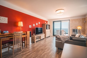 Ein modernes Wohnzimmer mit Fernseher, Holzmöbeln und einem Balkon mit Blick.