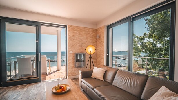 A modern room with a leather sofa, a wooden coffee table with fruit, and a large window overlooking the sea. - Villa Friede-Marie, App. Baltic Sea view - with fantastic sea view - Villa (Sassnitz auf Rügen)