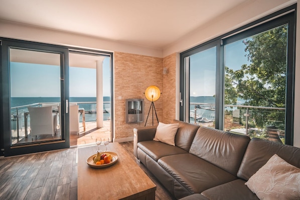 Ein modernes Zimmer mit einer Ledersofa, einem Couchtisch mit Früchten und einem großen Fenster mit Meerblick.