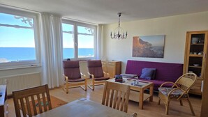 Un salon avec vue sur la mer, une table à manger, des chaises, un canapé et une bibliothèque.