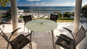 Une table ronde en verre, quatre chaises, un saladier en verre et une vue sur la mer et un pont.