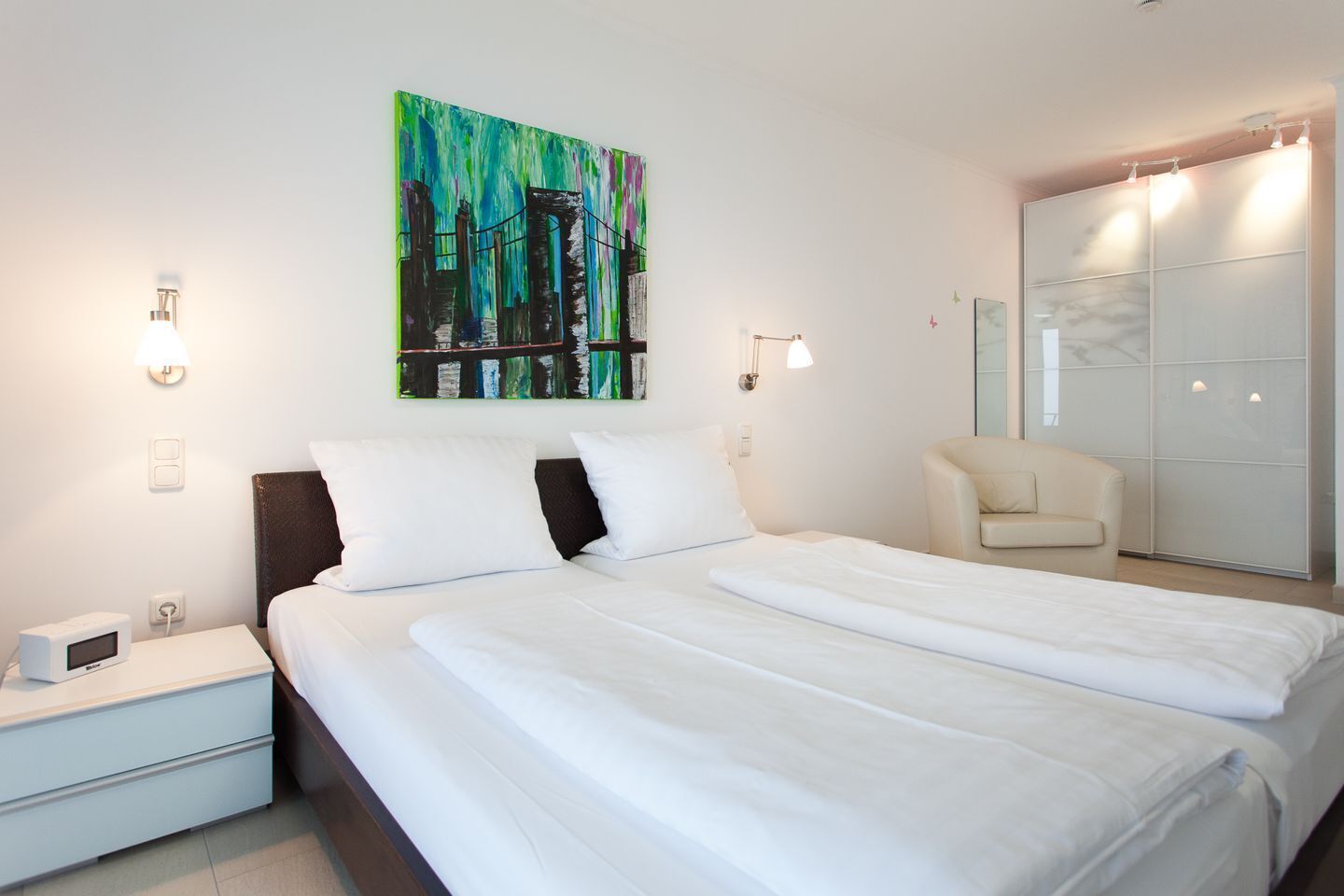 Ein Hotelzimmer mit Bett, Nachttisch, Lampe, Kunstwerk und einem Schiebetürenschrank.