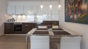 Une cuisine moderne dotée d’un îlot central, d’un coin repas avec une table et des chaises, et d’un grand tableau abstrait accroché au mur.