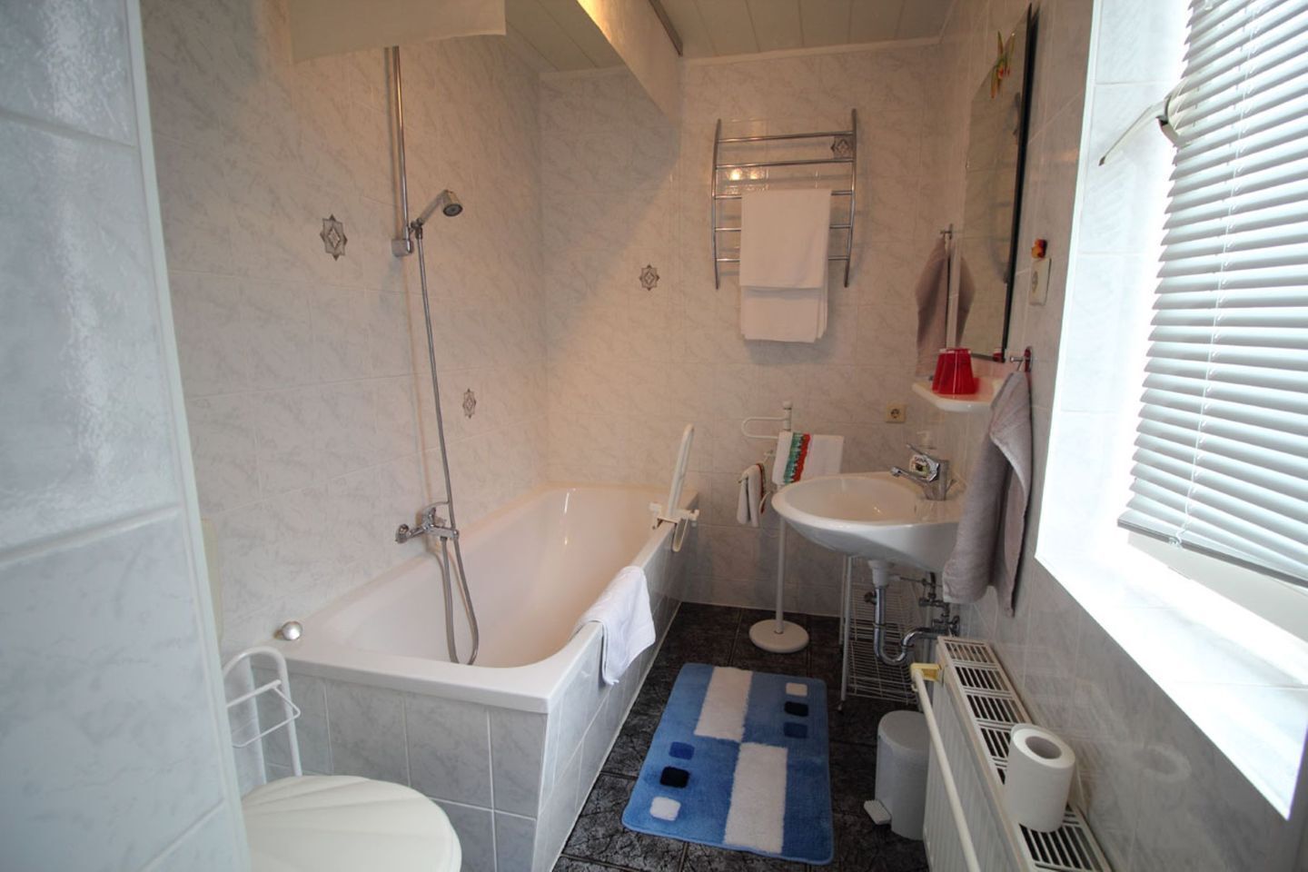 Ein Badezimmer mit Badewanne, Toilette, Waschbecken und einem Fenster mit Jalousien.