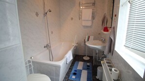 A bathroom with a bathtub, toilet, sink, and a window with blinds. - Apartment Thurk - centrally located in the harbor town of Sassnitz (Sassnitz auf Rügen)