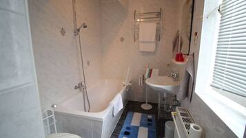 Ein Badezimmer mit Badewanne, Toilette, Waschbecken und einem Fenster mit Jalousien.