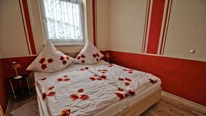 A bed with a floral bedspread, two pillows, a bedside lamp, and a window with a view. - Apartment Thurk - centrally located in the harbor town of Sassnitz (Sassnitz auf Rügen)