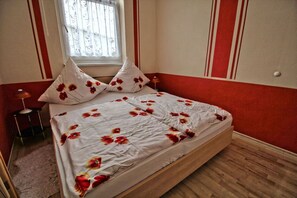 A bed with a floral bedspread, two pillows, a bedside lamp, and a window with a view. - Apartment Thurk - centrally located in the harbor town of Sassnitz (Sassnitz auf Rügen)