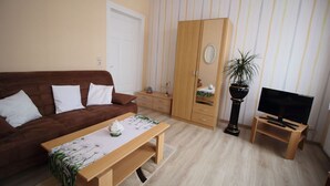 A living room with a brown sofa, a wooden coffee table, a TV on a stand, a wardrobe, and a potted plant. - Apartment Thurk - centrally located in the harbor town of Sassnitz (Sassnitz auf Rügen)