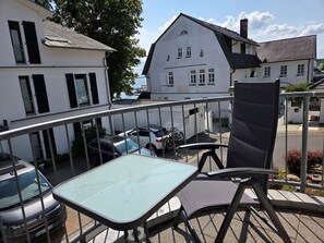 A balcony with a table and chairs, overlooking a street with parked cars and buildings. - Feuerstein vacation apartment - near the harbor (Sassnitz auf Rügen)