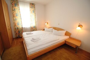 Ein Doppelbett mit weißen Bettwäsche, zwei Nachttischlampen, ein Nachttisch aus Holz und ein Kleiderschrank.