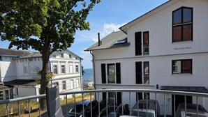 Un balcon avec une table et des chaises, donnant sur des voitures garées et un immeuble portant l’inscription « Villa Friede-Marie ».