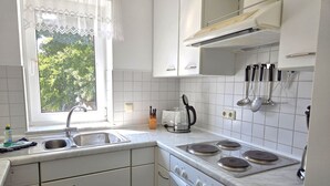 Une cuisine avec des meubles blancs, un évier, une cuisinière et une fenêtre donnant sur un paysage verdoyant.