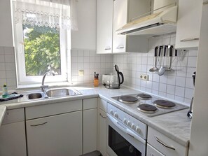 Eine Küche mit weißen Schränken, einer Spüle, einem Herd und einem Fenster mit Blick auf Grünflächen.