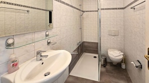 Ein Badezimmer mit weißem Waschbecken, Glasregal, Dusche, Toilette und Spiegel.