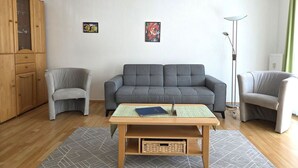 Un salon avec un canapé gris, deux fauteuils, une table basse en bois et un lampadaire.