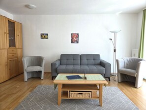Ein Wohnzimmer mit grauem Sofa, zwei Sesseln, einem Holztisch und einer Stehlampe.