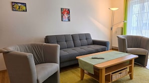 Ein Wohnzimmer mit grauem Sofa, einem Holztisch und einer Stehlampe.
