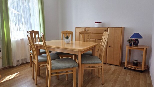 Un coin repas comprenant une table et des chaises en bois, un petit meuble et une table d’appoint avec une lampe.