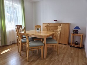 A dining area with a wooden table and chairs, a small cabinet, and a side table with a lamp. - Feuerstein vacation apartment - near the harbor (Sassnitz auf Rügen)