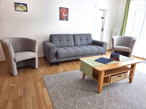A living room with a grey sofa, two armchairs, a wooden coffee table, and a patterned rug. - Feuerstein vacation apartment - near the harbor (Sassnitz auf Rügen)