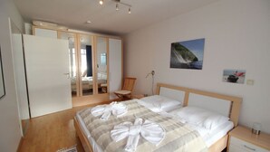 A bedroom with a bed, bedside tables, a chair, a wardrobe, and a painting on the wall. - Villa Prinz Heinrich - App.3 with balcony and Baltic Sea view - Villa Prinz Heinrich, (Sassnitz auf Rügen)