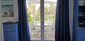 Ein Zimmer mit einer Schiebetür zu einer Terrasse im Freien mit weißem Zaun, Korbstühlen und einem Tisch.