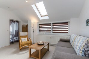 Ein Wohnzimmer mit hoher Decke, einem Dachfenster, einem Sofa, einem Sessel, einem Tisch und einer Heizung.