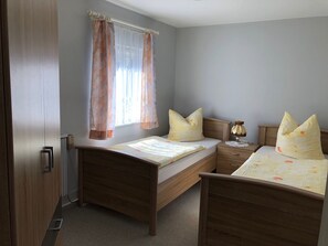 Ein Schlafzimmer mit zwei Holzbett, einem Nachttisch, einer Lampe und einem Fenster mit Vorhängen.