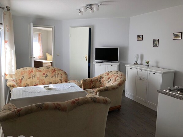 Ein Zimmer mit einem Bett, zwei blumengemusterten Sofas, einem Fernseher auf einem Schrank und einer kleinen Küchenzeile.