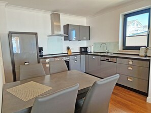 Eine moderne Küche mit Edelstahlgeräten, ein Essbereich mit Tisch und Stühlen sowie ein Fenster mit Blick auf ein Haus.