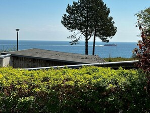 Ein Gebäude mit einem geneigten Dach, Blick auf das Meer und ein Schiff in der Ferne.