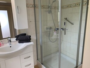 Ein Badezimmer mit einer Duschkabine, einem weißen Waschbecken mit Spiegel und einem Handtuchhalter.