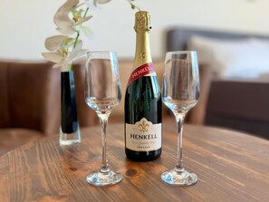 Una botella de vino Henkell Trocken y dos copas de vino vacías sobre una mesa de madera.