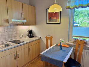 A compact kitchen with wooden cabinets, a coffee maker, a sink, and a window with a view of greenery.
