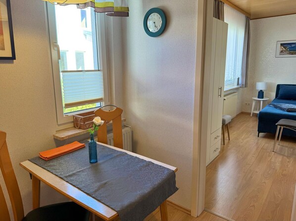 A compact room with a dining table, a small chair, a clock on the wall, and a bed with a blue bedspread. - Vacation home Seeblick in Sassnitz on Rügen with terrace (Sassnitz auf Rügen)