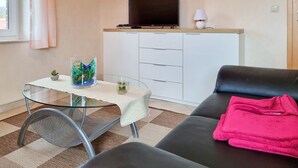 A living room with a glass table, a sofa, a TV on a cabinet, and a small plant. - Johanna vacation apartment - located on the Wieker Bodden (Wiek auf Rügen)