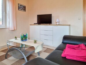 A living room with a glass table, a sofa, a TV on a cabinet, and a small plant. - Johanna vacation apartment - located on the Wieker Bodden (Wiek auf Rügen)