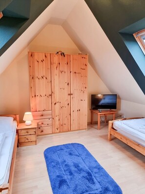 A bedroom with a sloped ceiling, wooden wardrobe, two beds, a TV, and a blue rug. - Johanna vacation apartment - located on the Wieker Bodden (Wiek auf Rügen)