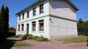 A two-story building with a symmetrical facade, a central entrance with steps, and a small porch area. - Vacation apartment Vieth in Sassnitz on Rügen with seating area in the garden (Sassnitz auf Rügen)