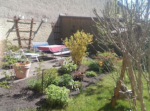 Ein Gartenbereich mit Holzbank, Tisch mit rotem Tischläufer und verschiedenen Blumentöpfen.