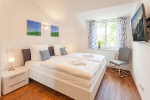 A bedroom with a bed, bedside tables, a chair, a window with curtains, and wall art. - Villa Am alten Kreidebruch - Penthouse Sea Spirit - Villa Am alten Kreidebruch, (Sassnitz auf Rügen)