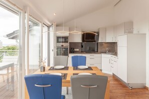 A modern kitchen with white cabinets, a dining table with blue and gray chairs, and a view through a glass door to an outdoor deck. - Villa Am alten Kreidebruch - Penthouse Sea Spirit - Villa Am alten Kreidebruch, (Sassnitz auf Rügen)