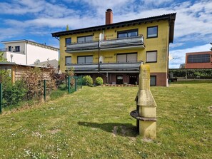 Ein zweistöckiges, gelbes Geb äude mit Balkon, umgeben von einem Rasen und einem Zaun.