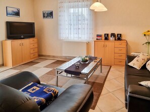 Ein Wohnzimmer mit einer Couch, einem Couchtisch, einem Fernseher, Lautsprechern und einer Heizung.